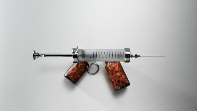 a syringe lying across two bottles of pills, tablets, so as to imitate the shape of a gun