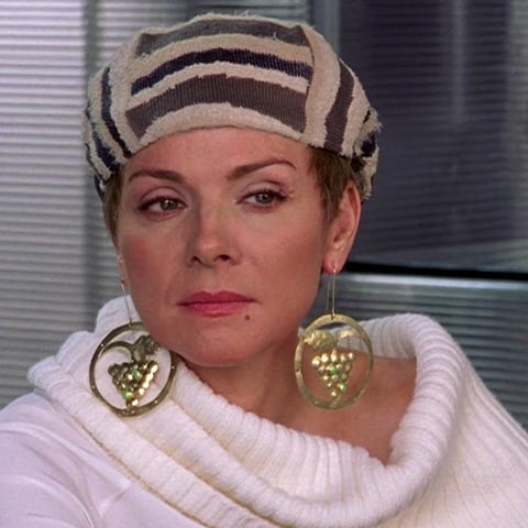 samantha in a white sweater, hat, and grape earrings