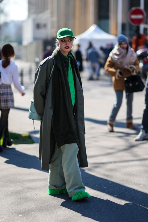 paris, france march 08 a guest wears a green cap, silver earrings, a dark green ribbed wool high neck pullover, a green tie, a dark green oversized long coat, a pale blue shiny leather tube shoulder bag, pale blue denim wide legs pants, neon green fluffy shoes , outside miu miu , during paris fashion week womenswear fw 2022 2023, on march 08, 2022 in paris, france photo by edward berthelotgetty images