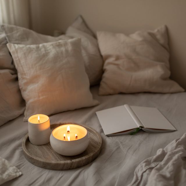 scented candles in ceramic bowls on linen bed with book at home