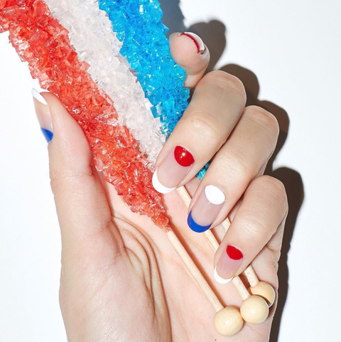 a hand holding candy with a manicure, featuring negative space and red, white and blue colors