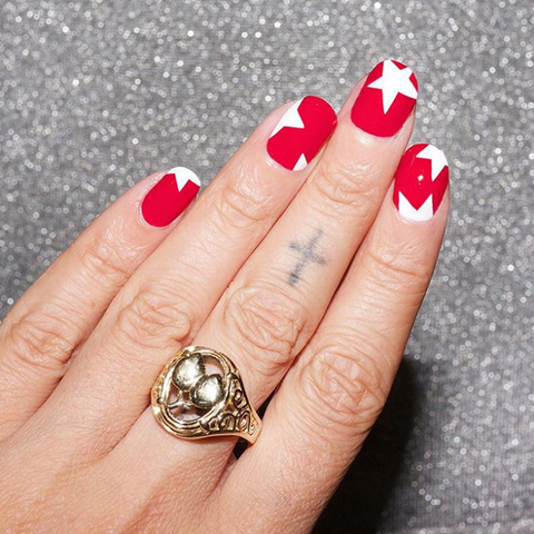 a manicure with a red base and white star designs, featuring a gold ring on a grey background