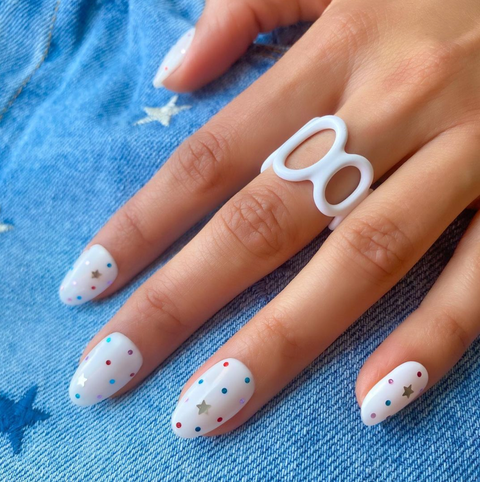 a white manicure with colorful star and polka dot designs on a denim background