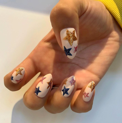 nails with a nude base, featuring pink, blue, and gold stars on each fingernail