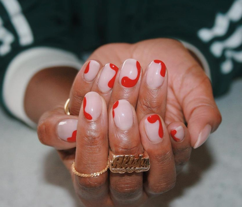 hands wearing gold rings and pink nude nails with red squiggly, swirl designs