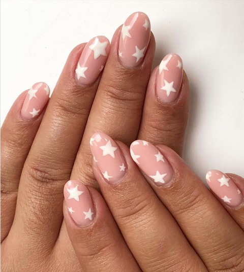 two hands are stacked on top of each other, featuring a manicure with a pink nude base and various shaped white stars