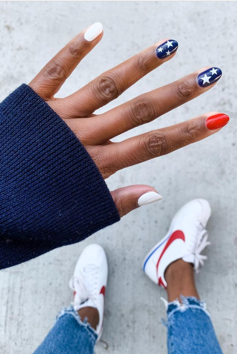 a manicure that features various designs on each fingernail, like a white base, a blue base with a few white stars and a red base