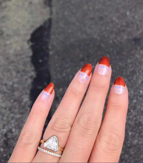 a hand with a diamond ring, featuring a clear manicure with a blue line and red block tips on a grey background