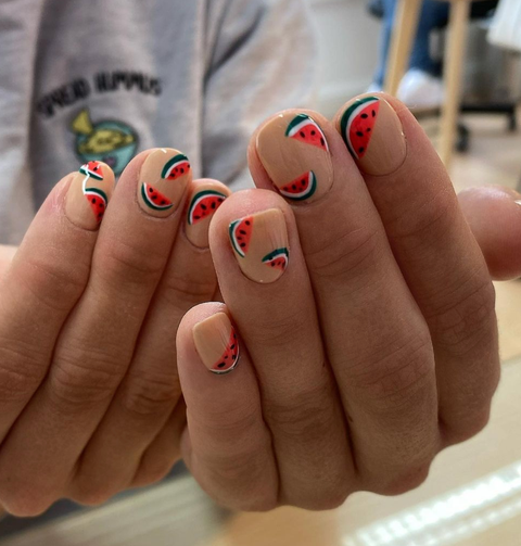 a nude manicure, featuring a unique red, black, white, and green watermelon design on each fingernail