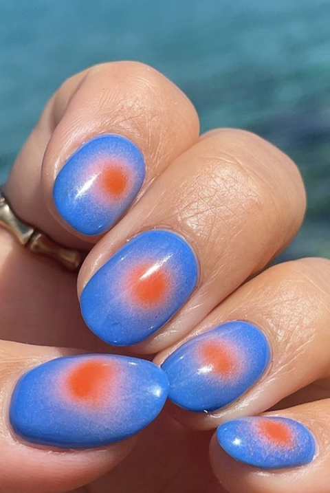 a blue manicure with a red ombre circle design on a blue background