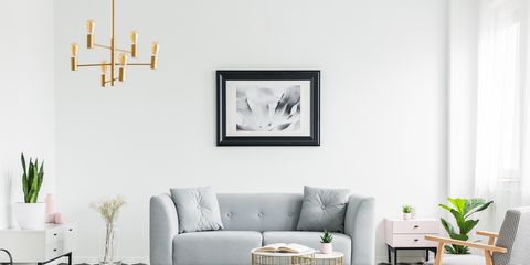 Poster above grey sofa in bright patterned living room interior with armchair and gold lamp. Real photo