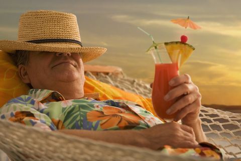 senior man lying in hammock with tropical drink, smiling