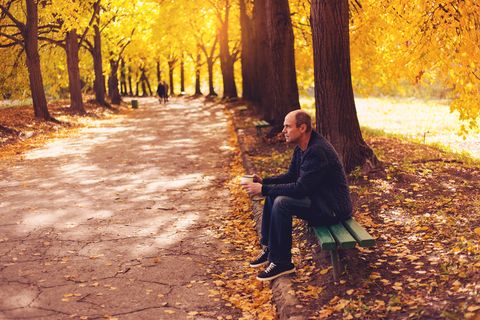 Senior man sitting on bench with hot drink in  autumn park