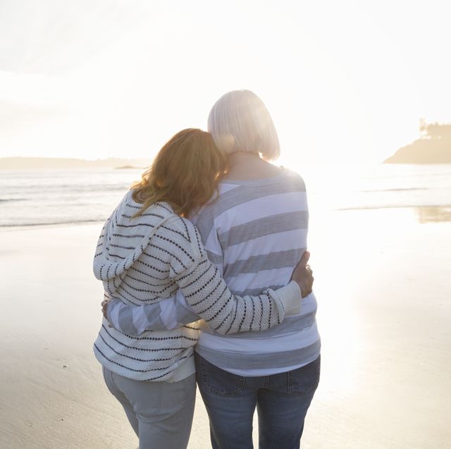 senior woman and daughter hugging on beach looking at ocean view at sunset