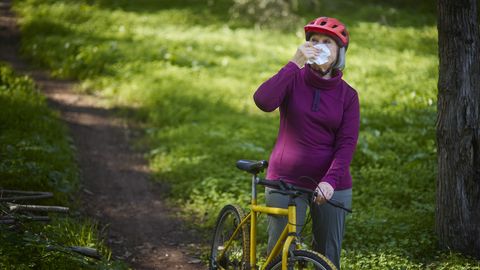 vrouw houdt fiets vast terwijl ze haar neus snuit