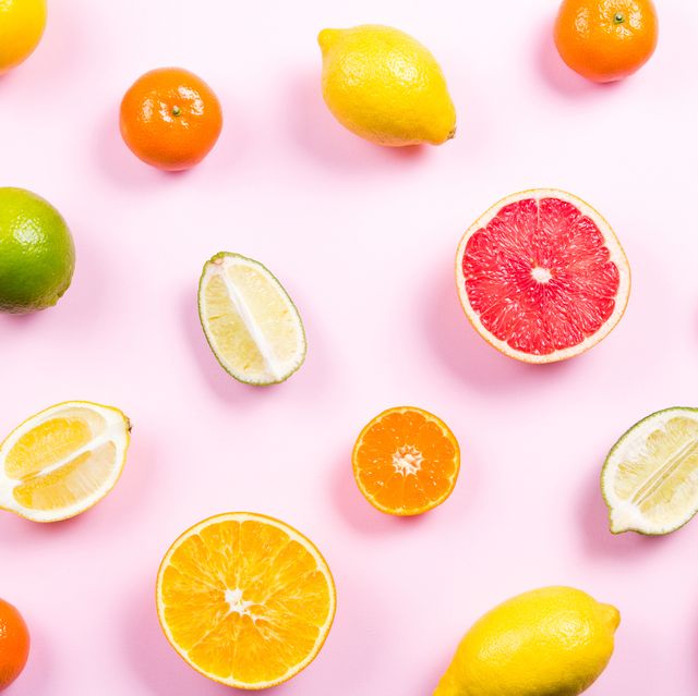 Several kinds of whole and cut citrus on a pink background