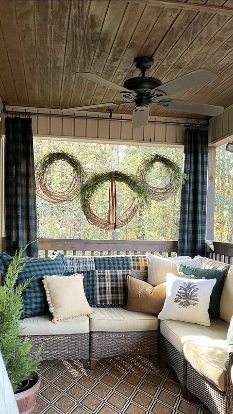 a front porch with a sofa decorated with throw pillows and wreaths above