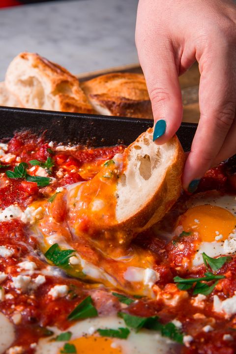 piece of bread being dipped into tomato and egg shakshuka