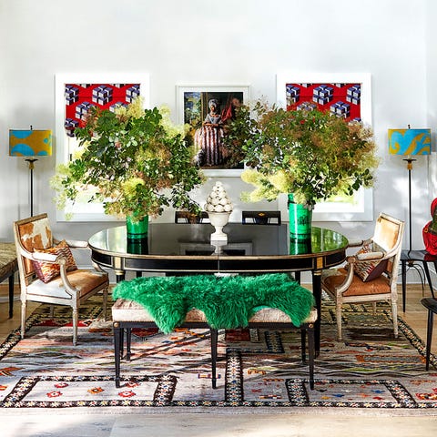 dining area with large oval table carpet below large vases with green flowers and artwork hanging on the walls