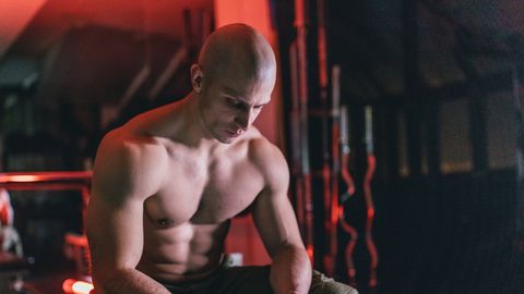 Shirtless body builder sitting on bench in dark gym
