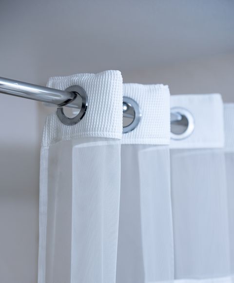 white shower curtain hanging from a chrome shower curtain rod