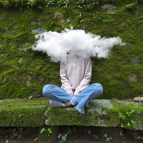 woman sitting on rock with a cloud over her face