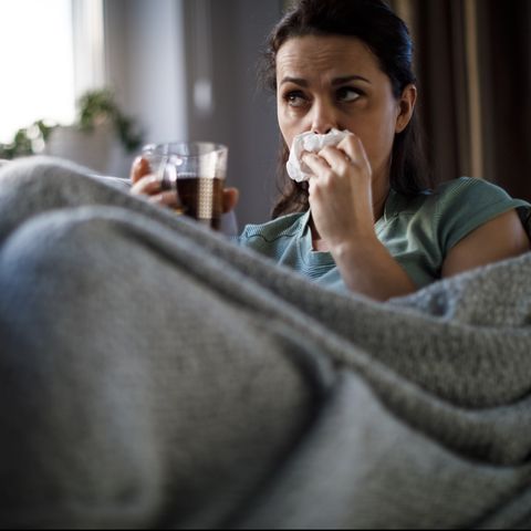sick woman lying in bed and blowing nose