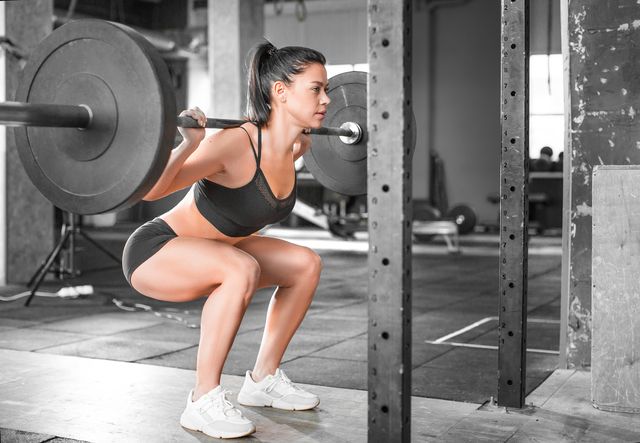 side view of a woman in the gym hard training squat