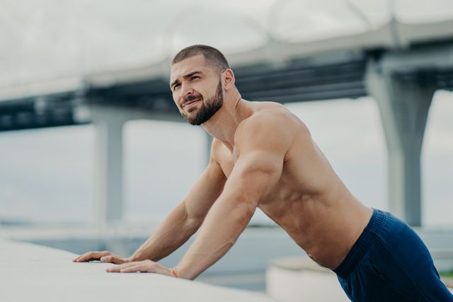 side view of shirtless young man exercising on retaining wall