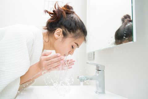 side view of young woman washing face in bathroom at home