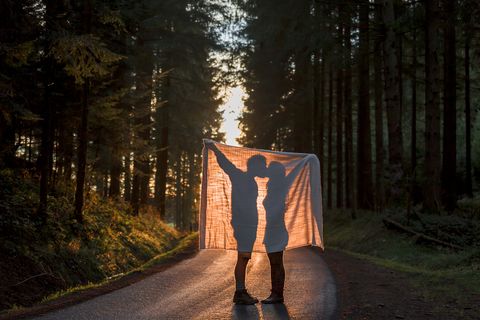 silhouette of couple holding blanket kissing on country road in forest