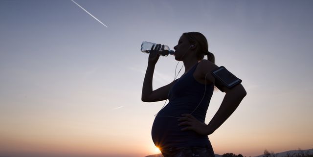 silhouette of pregnant woman drinking water from bottle at sunset