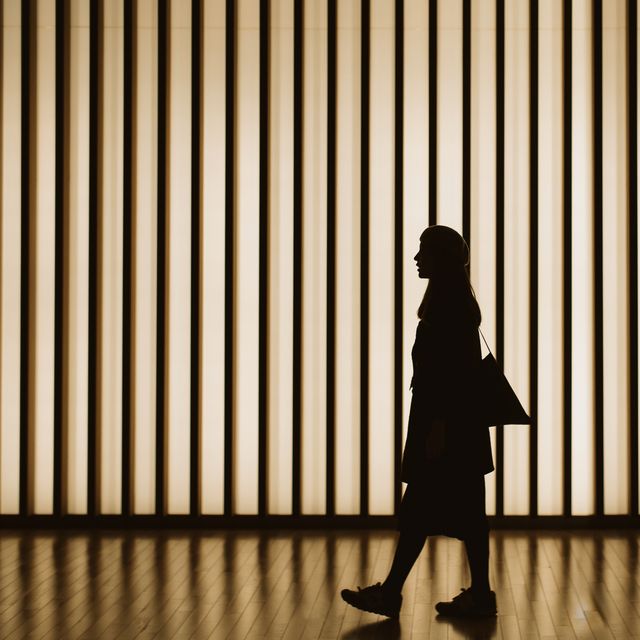 silhouette of woman walking in front of striped illuminated wall