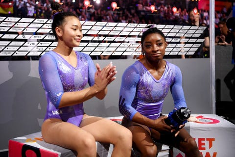 simone biles and sunisa lee sitting side by side in purple and silver leotards during a competition