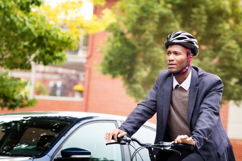 Single black male in his 30s cycling past car with helmet