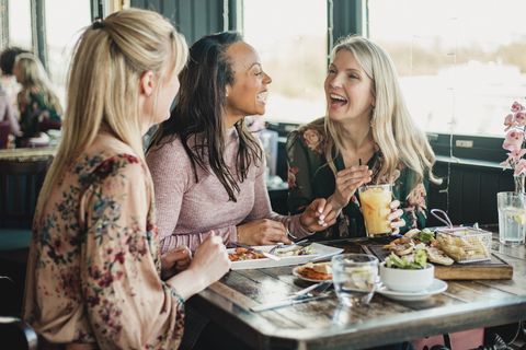 a front view shot of three beautiful mid adult women enjoying brunch together in a restaurant, they are sitting around a table and laughing with eachother
