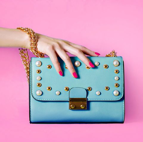 Sky blue handbag purse and beautiful woman hand with red manicure isolated on pink background.