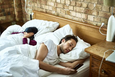 Woman fast asleep next to partner who is checking his smartphone