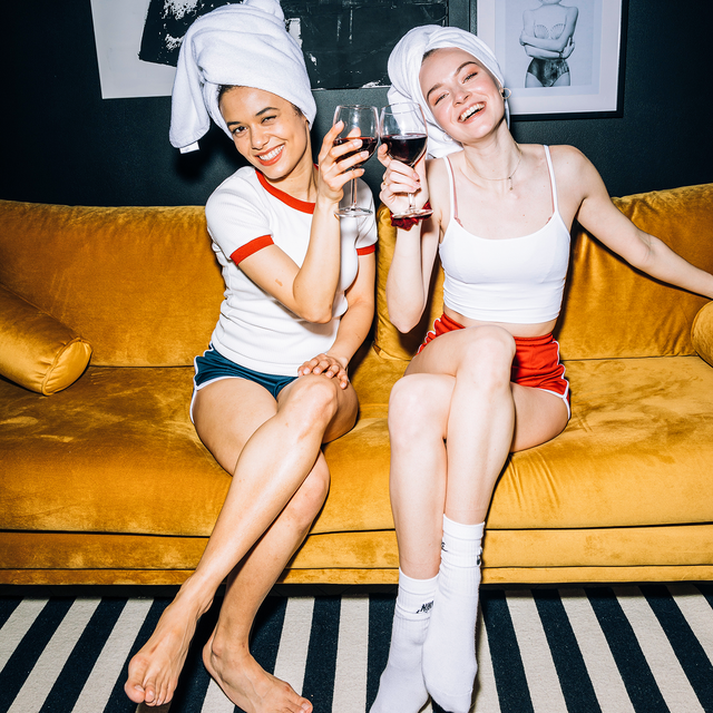 two smiling women sitting on a couch with their hair in towels and holding wine glasses