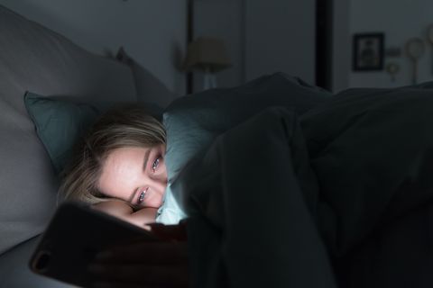 sleepy tired woman lying in bed under the blanket using mobile phone at night insomnia addiction