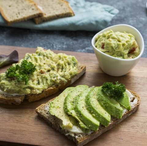 Slices of bread with sliced avocado and avocado cream on wooden board