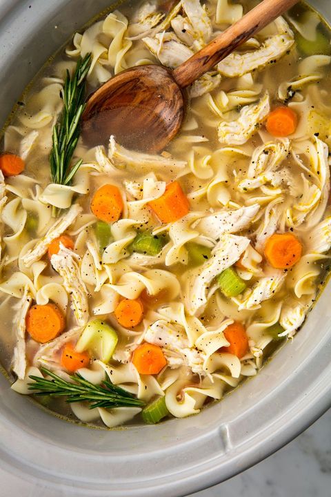 close up of chicken noodle soup garnished with fresh rosemary in a slow cooker