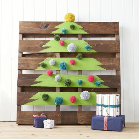 a shipping pallet rests against the wall and a green tree shape is painted on and there are pom pom decorations draped across