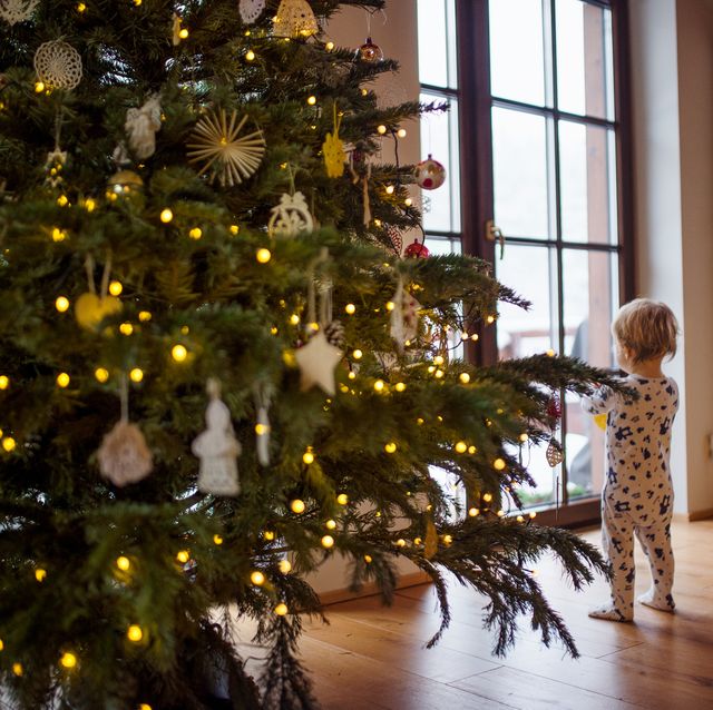 A small girl in sleepsuit indoors at Christmas time, looking out through window.
