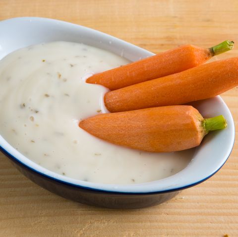 healthy eating small raw carrots or natural baby carrots in a small recipient full of ranch dressing