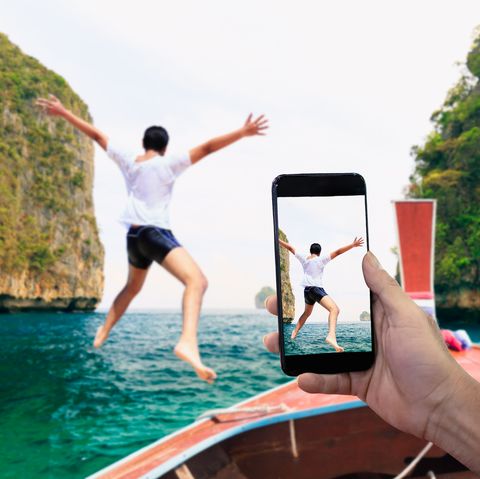 Smartphone photographing Asian young man jumping from boat into the Andaman Sea, Thailand