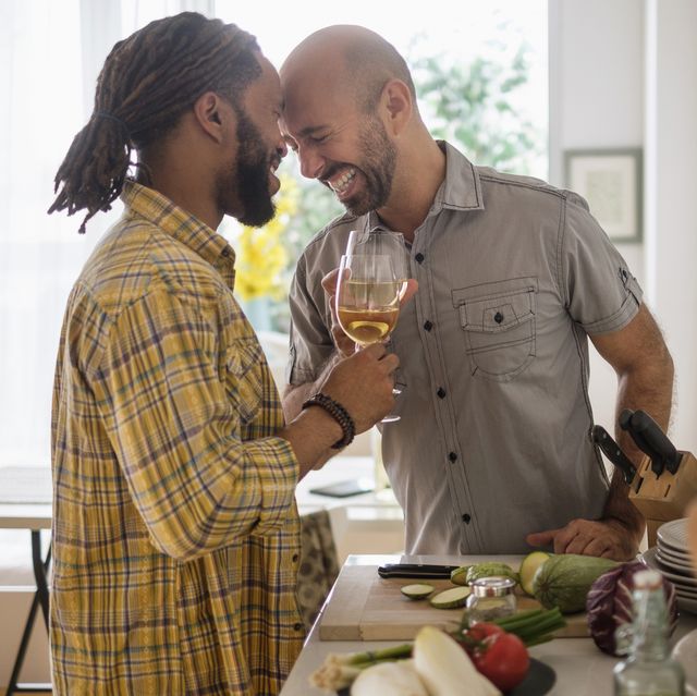 smiley homosexual couple drinking wine in kitchen