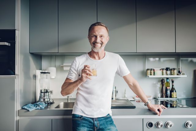 smiling bearded midaged man holding glass in kitchen