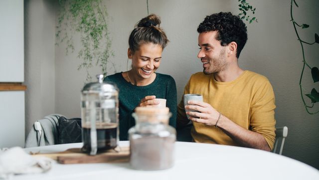 smiling boyfriend and girlfriend having coffee at table in living room