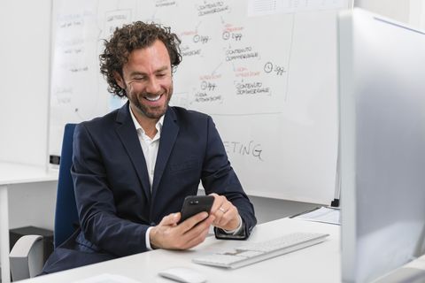 Smiling businessman sitting at desk in office using cell phone
